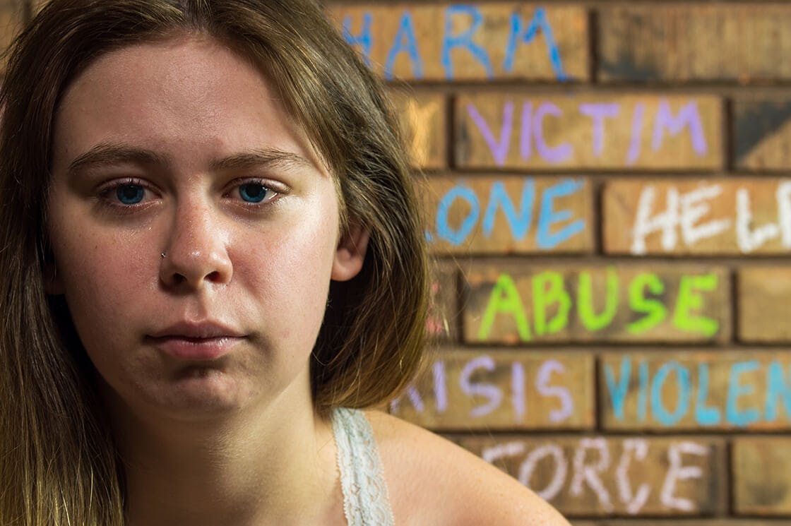 Teenage girl crying in front of a wall with abusive words written on it