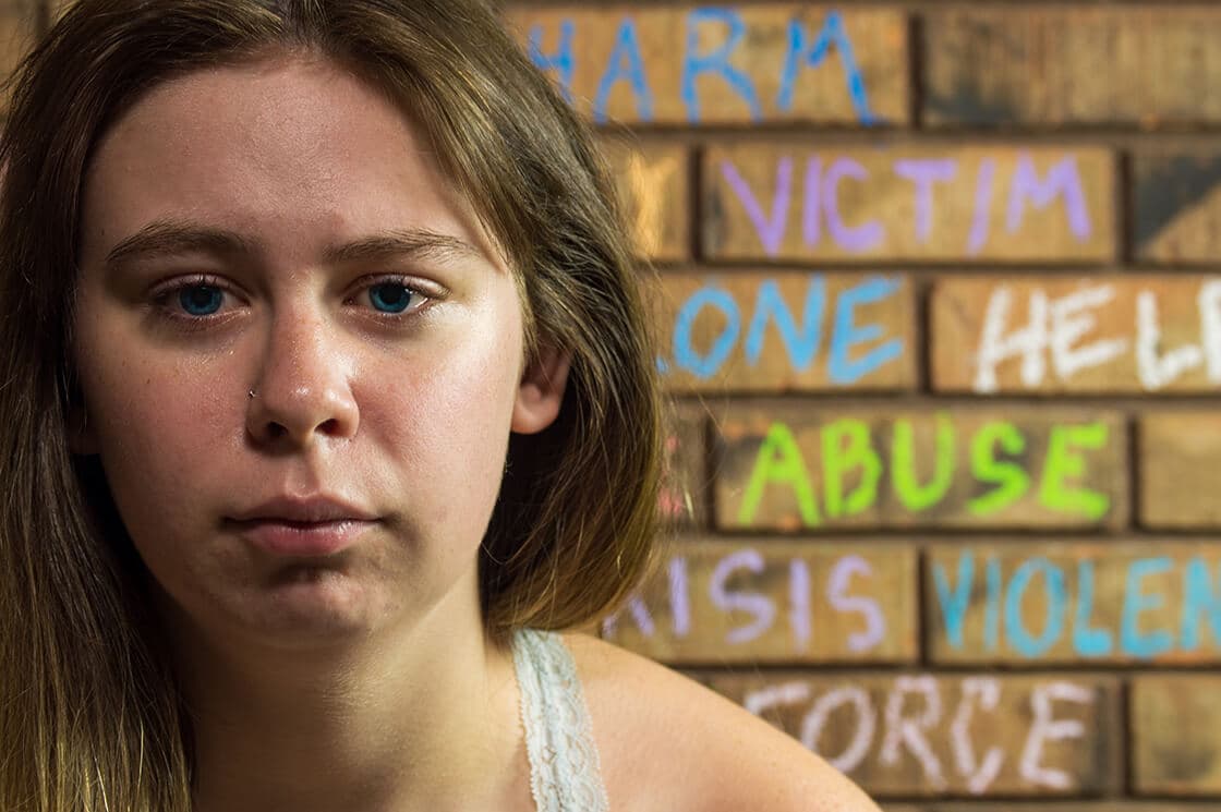 Teenage girl crying in front of a wall with abusive words written on it