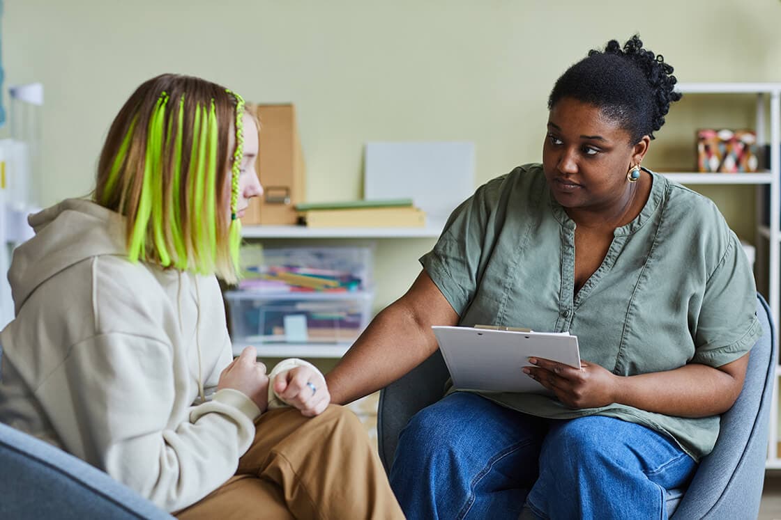 A woman medical professional comforting a younger girl and filling out papers